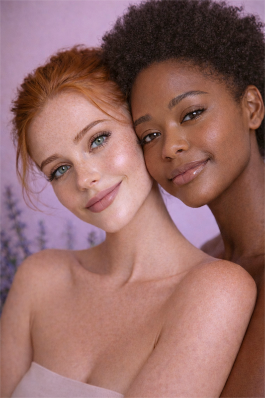 Two women with radiant skin posing together in a natural skincare photoshoot, representing the Gentle Roots lavender face and body balm.
