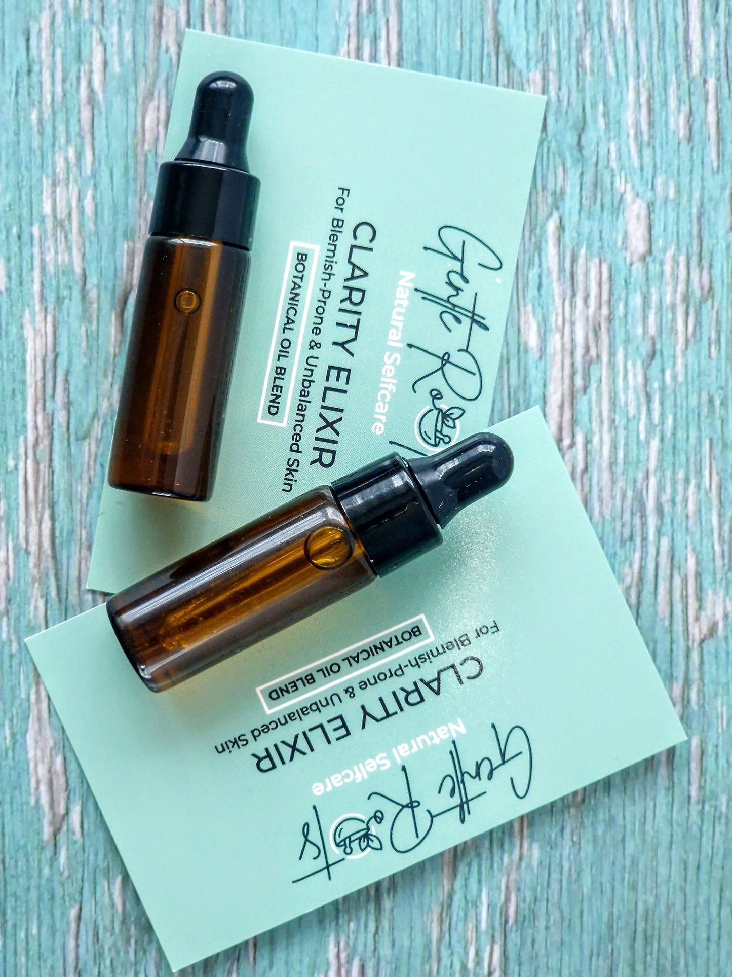 Two amber glass bottles with black caps on green cards labeled 'Clarity Elixir' on a light blue wooden surface.