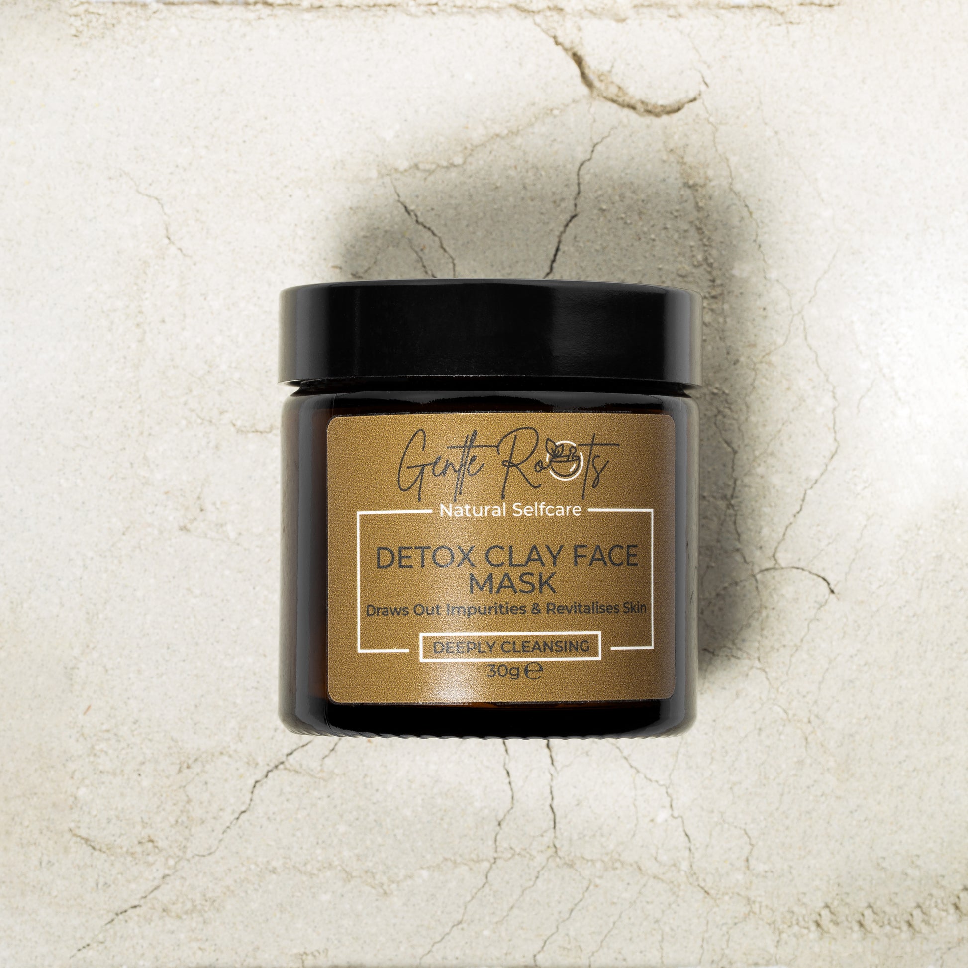 Gentle Roots Detox Clay Face Mask in amber glass jar on a background of powdered clay