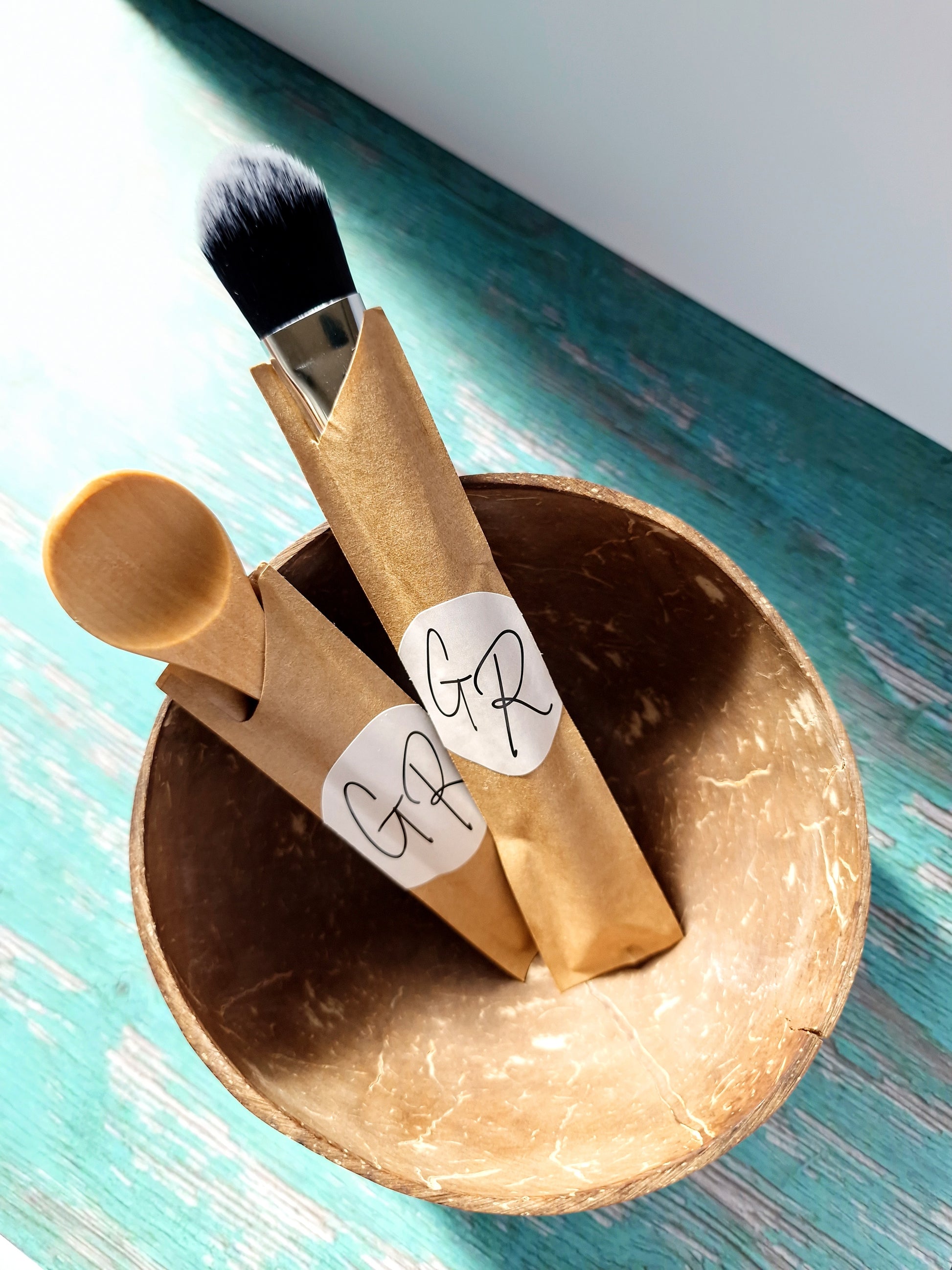 Bamboo masking brush and spoon resting inside coconut bowl – Gentle Roots Essentials Masking Kit.