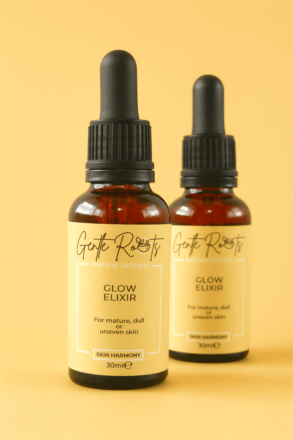 Pair of Gentle Roots Glow Elixir bottles on a yellow background – vegan, non-toxic face oil for dull and uneven skin.
